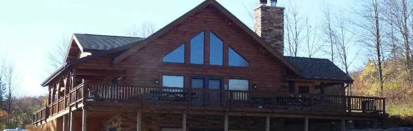 Log home exterior with large great room windows and stone chimney
