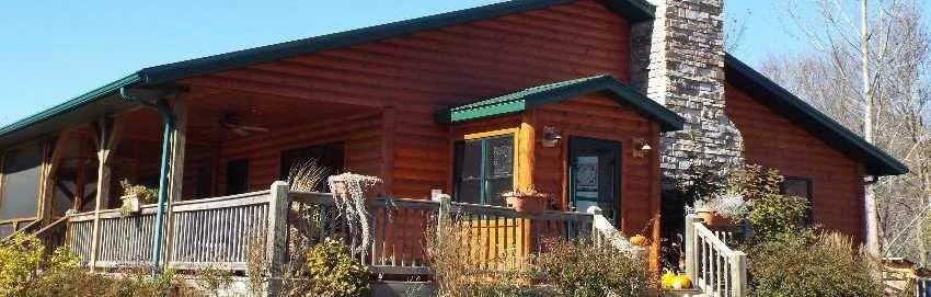 Maintained log home exterior with porch and stone chimney