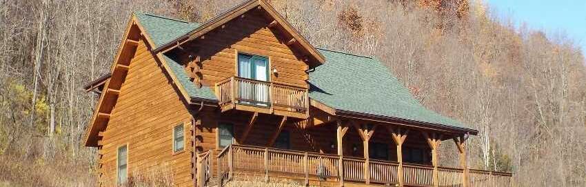 log home in sunlight in front of wooded hillside, crooked creek construction header image 1